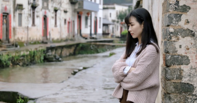 What Is Low Self-Esteem? Picture of person looking sad and staring into the distance. There are houses in the background and she is standing by a canal