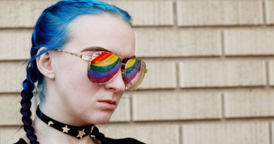 What is Asexuality? An 18 year old young person with blue hair in plaits wearing sunglasses with the pride flag reflecting in their sunglasses